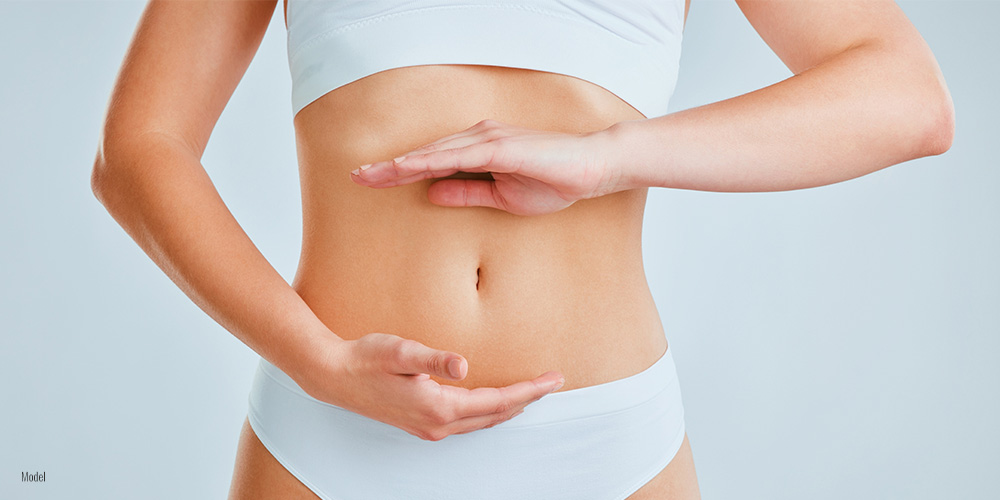 a woman wearing white undergarments frames her toned stomach with her hands